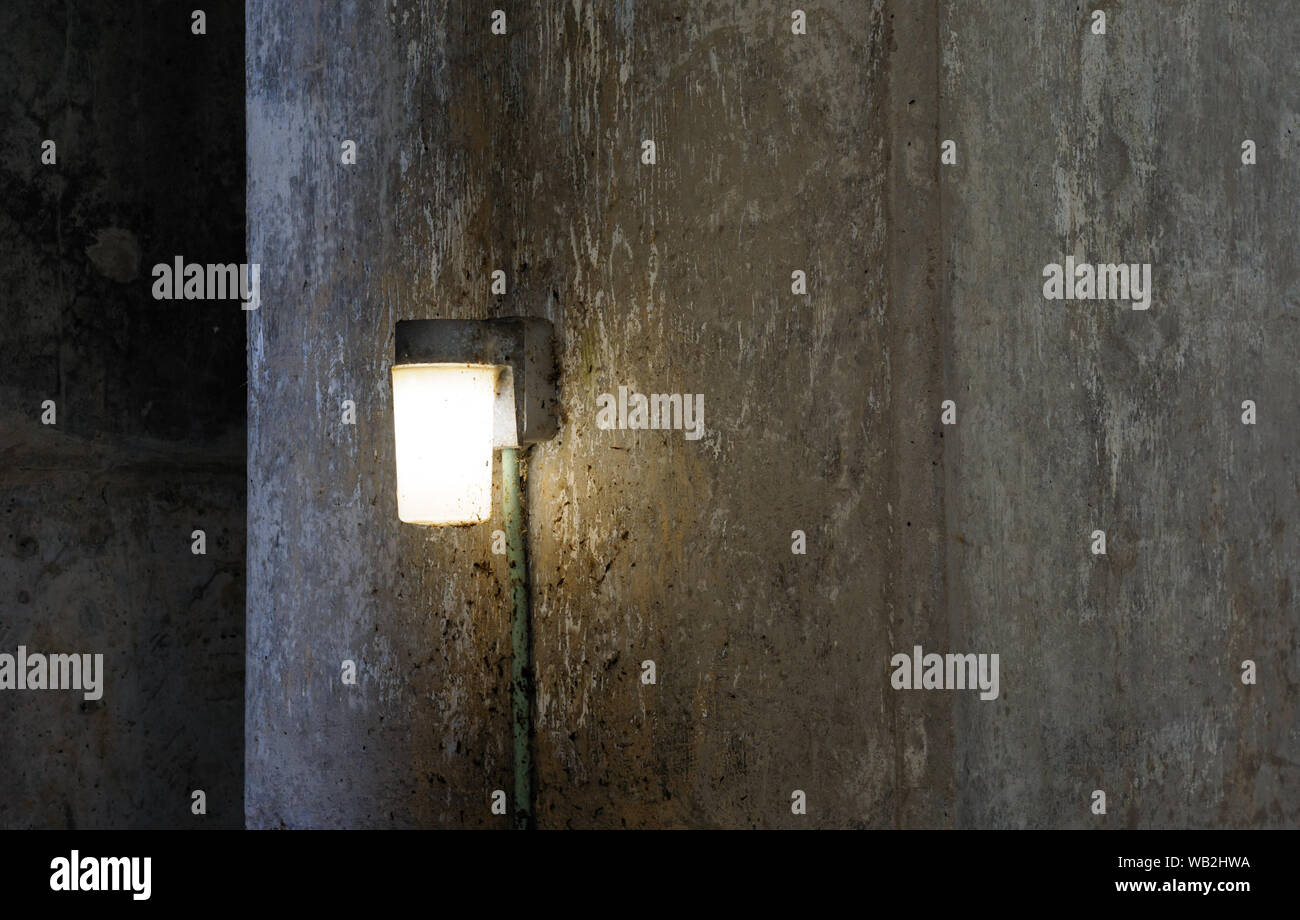 Singola lampada che brilla sulla buio sporco muro di cemento. Foto Stock