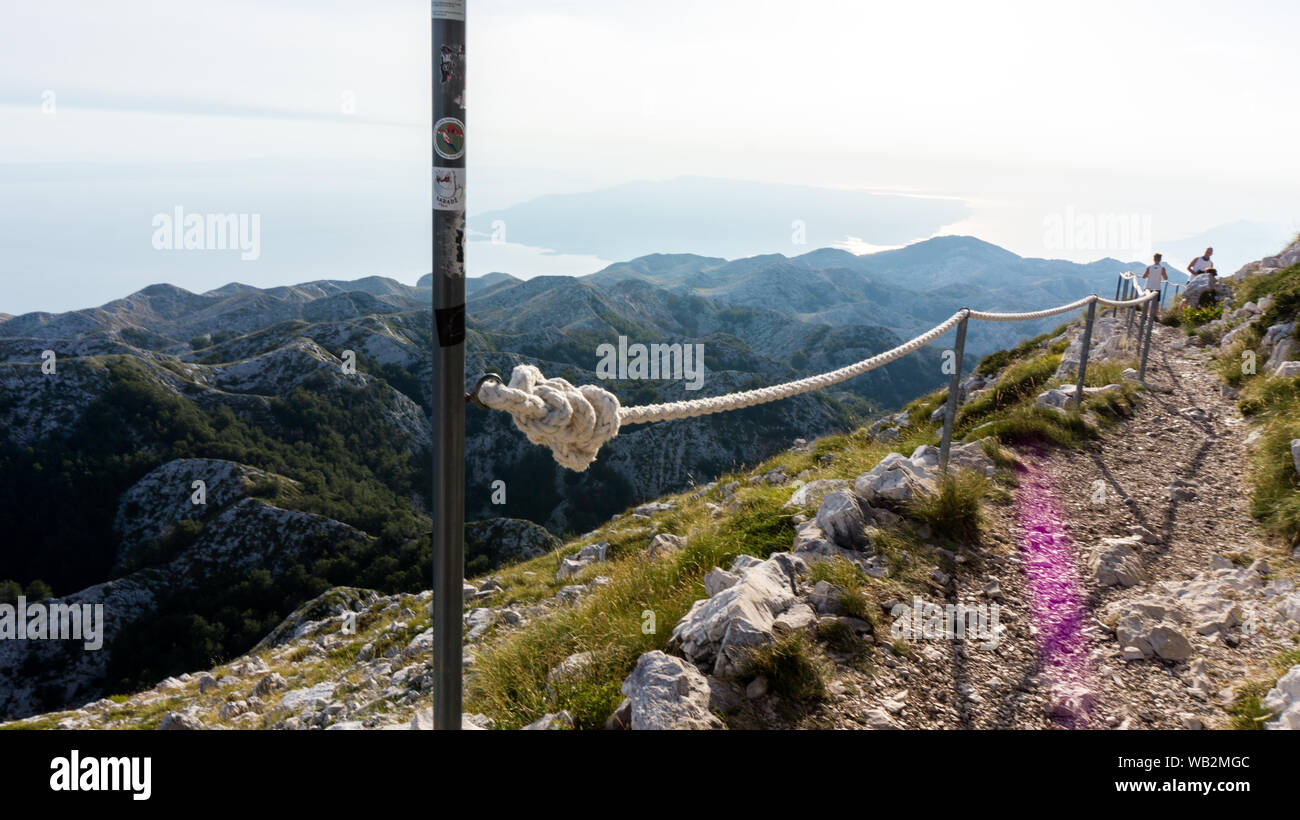 Makarska, Croazia - Agosto 13, 2019: via sassosa con fune recinzione, turisti in background, montagna Biokovo Foto Stock