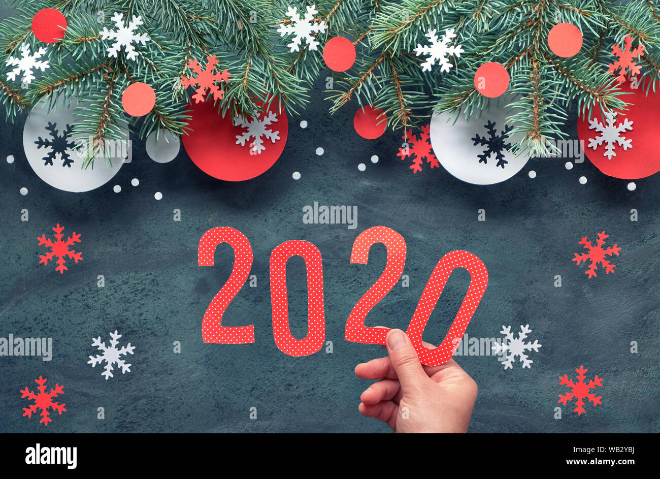 Mano azienda numero 2020, Natale sfondo con ramoscelli di abete rosso e bianco decorazioni di carta. Appartamento laico, vista dall'alto sulla astratta scuro dello sfondo. Foto Stock