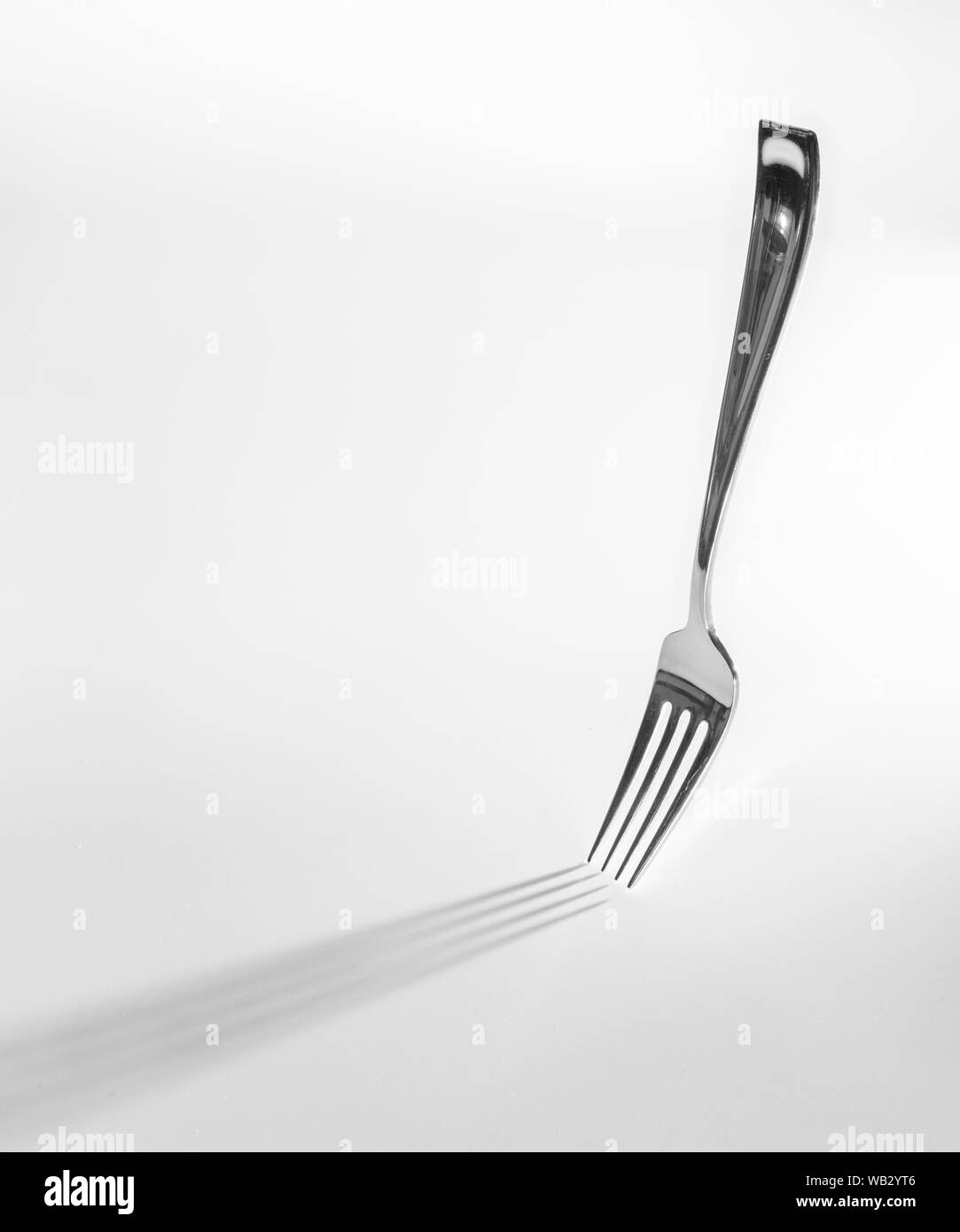 Una forcella si alza sul proprio la colata di una lunga ombra, isolata contro uno sfondo bianco Foto Stock