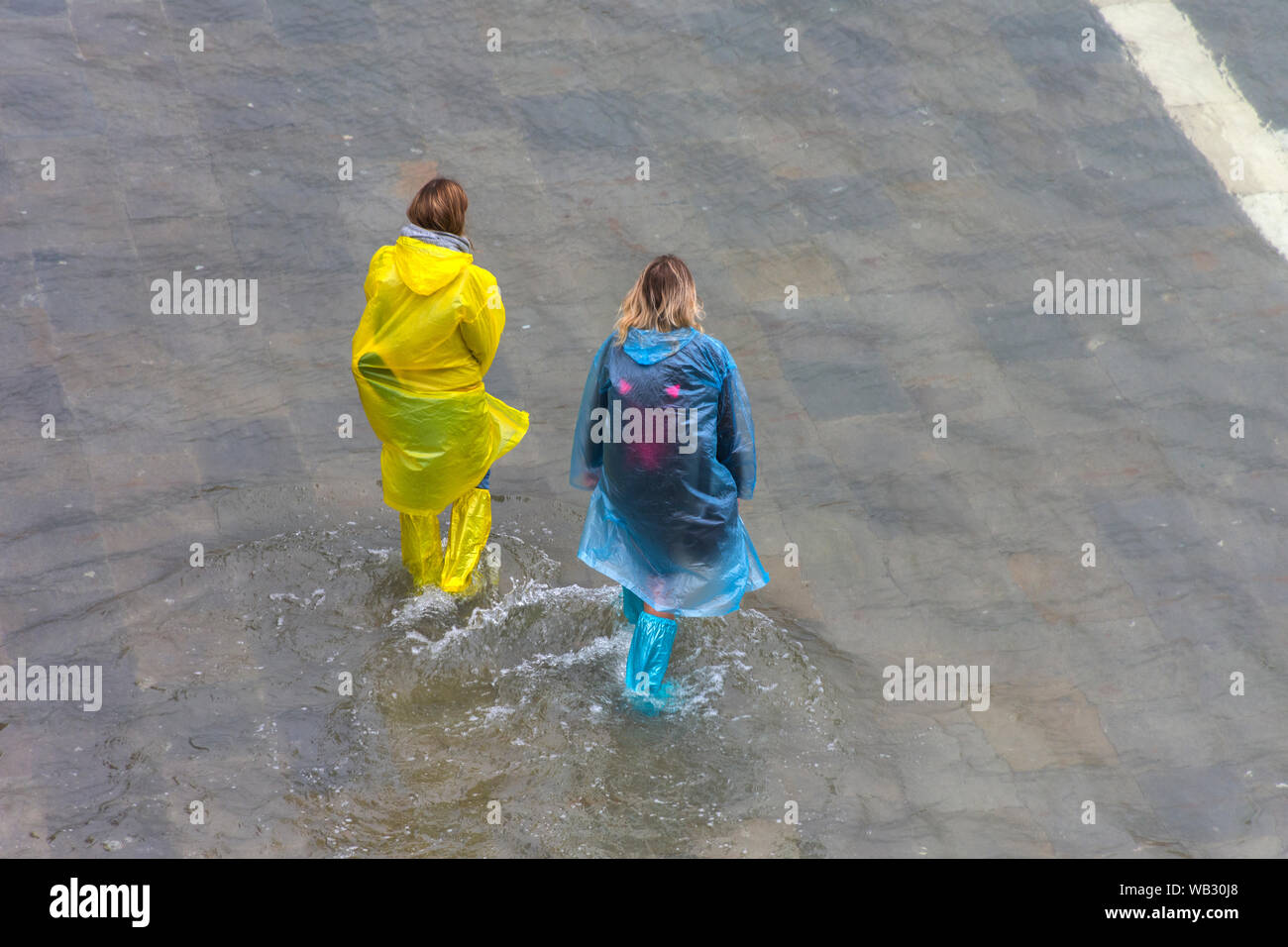 Due donne che indossano soprascarpe impermeabile a piedi attraverso acqua di inondazione durante un'acqua alta (l'acqua alta) evento, la Piazzetta di San Marco, Venezia, Italia Foto Stock