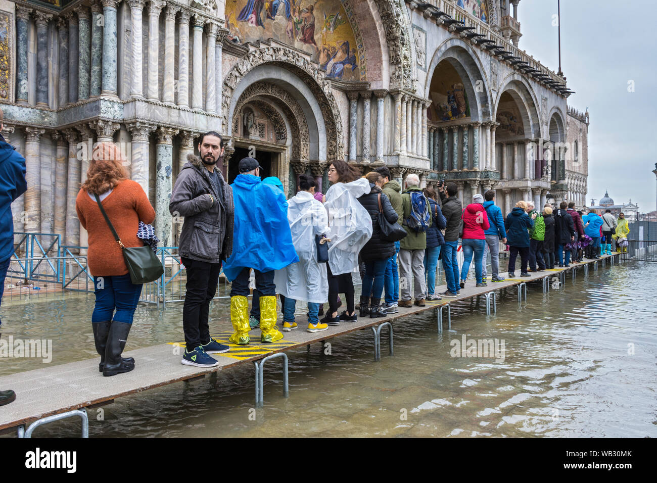 I turisti in coda su piattaforme elevate presso la Basilica di San Marco durante un'acqua alta alta (acqua), eventi di Piazza San Marco, Venezia, Italia Foto Stock