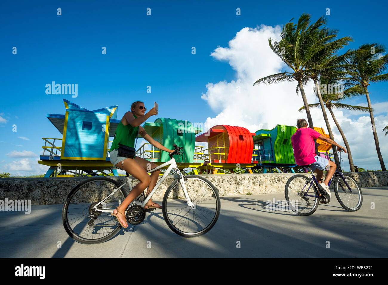MIAMI - 15 settembre 2018: un paio ride biciclette passato una fila delle colorate lifeguard torri in attesa di collocamento sulla spiaggia di South Beach. Foto Stock