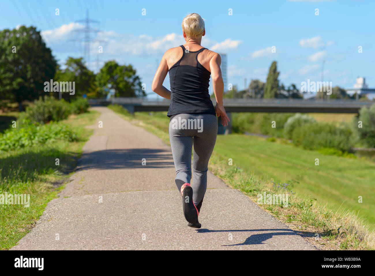 Montare donna sana godendo di un jog su un giorno di estate in un basso angolo di visione come lei passa la telecamera contro un cielo blu con spazio di copia Foto Stock