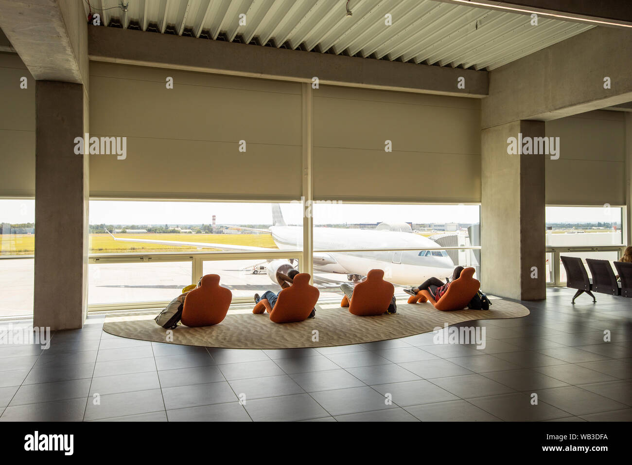 I viaggiatori rilassarsi sulle sedie a sdraio, guardando all'aeroporto di finestra. Irriconoscibile persone cercano in aereo, l'attesa. Aereo Aeroporto in attesa Foto Stock