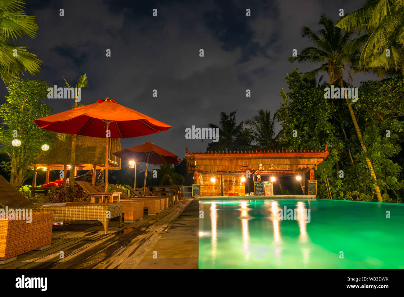 Foresta Pluviale con alberi di palma. Piscina senza persone con acqua retroilluminato. Lettini e ombrelloni. Notte. Il bar è chiuso Foto Stock