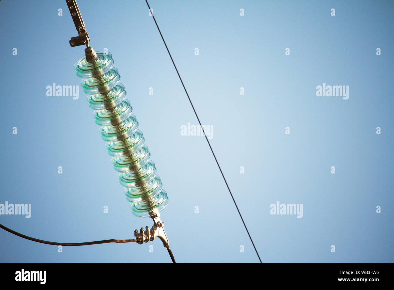 Chiudere la vista inferiore di isolatori su fili ad alta tensione su una torre di potenza contro un cielo blu Foto Stock