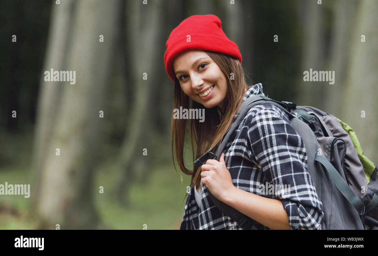 Allegro bruna ragazza turistica wearsing cappello e zaino avente camminare attraverso la foresta, il concetto di turismo Foto Stock