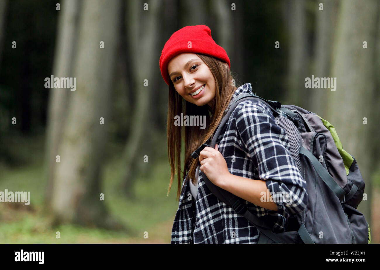 Felice donna sorridente con i capelli scuri porta zaino per il viaggiatore, godendo di giorno di estate e ammira la natura pittoresca luogo mozzafiato Foto Stock