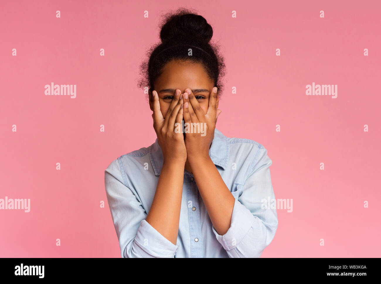 Ragazza timida che copre il viso con le mani e spiata attraverso le dita Foto Stock