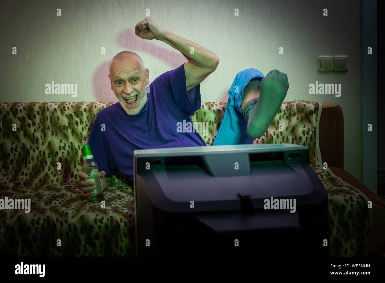 Un uomo adulto, tenendo una bottiglia in mano, orologi di una partita di calcio o altri sport, sulla televisione, mentre si beve, seduto su un divano. Egli è molto e Foto Stock