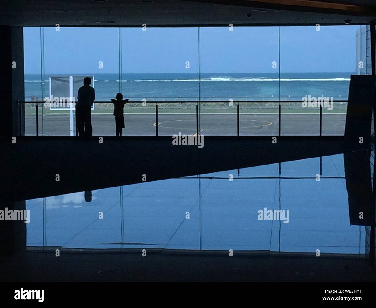 Silhouette di maschio e un bambino appoggiato contro la lancia si affaccia sulla finestra con vista sul mare Foto Stock