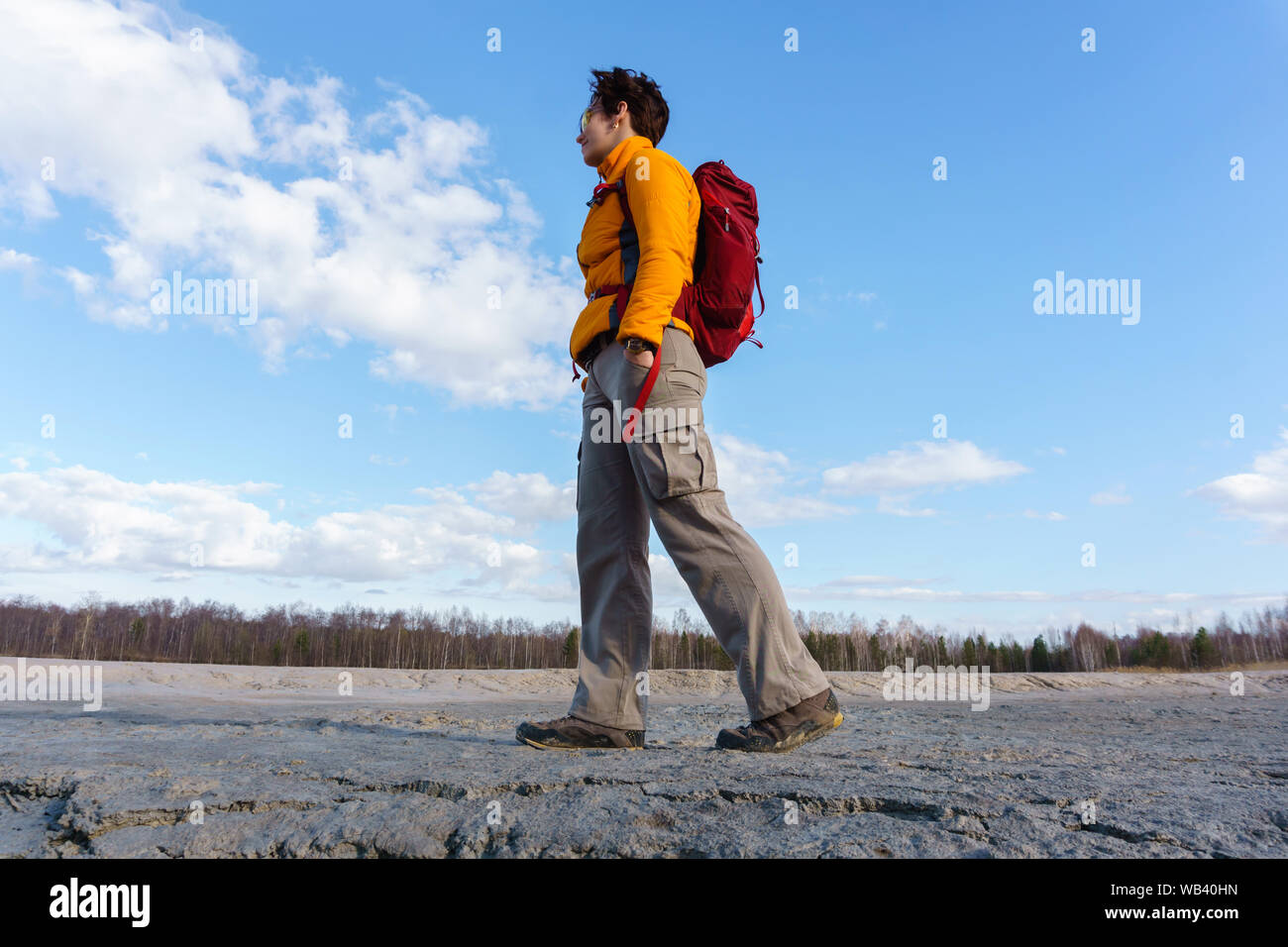 Donna traveler camminando in una zona desertica con la foresta di primavera all'orizzonte sotto un cielo blu con nuvole Foto Stock