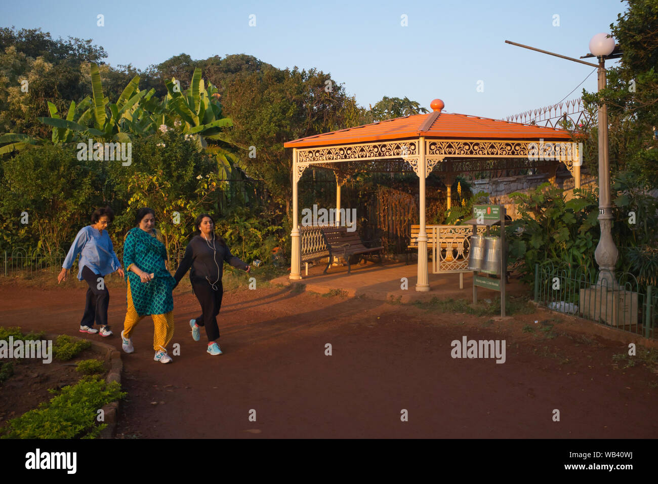 In un tardo pomeriggio, tre donne indiane power-a piedi passato un vecchio-stile pavilion al giardino pensile (Pherozeshah Mehta Gardens) in Mumbai, India Foto Stock