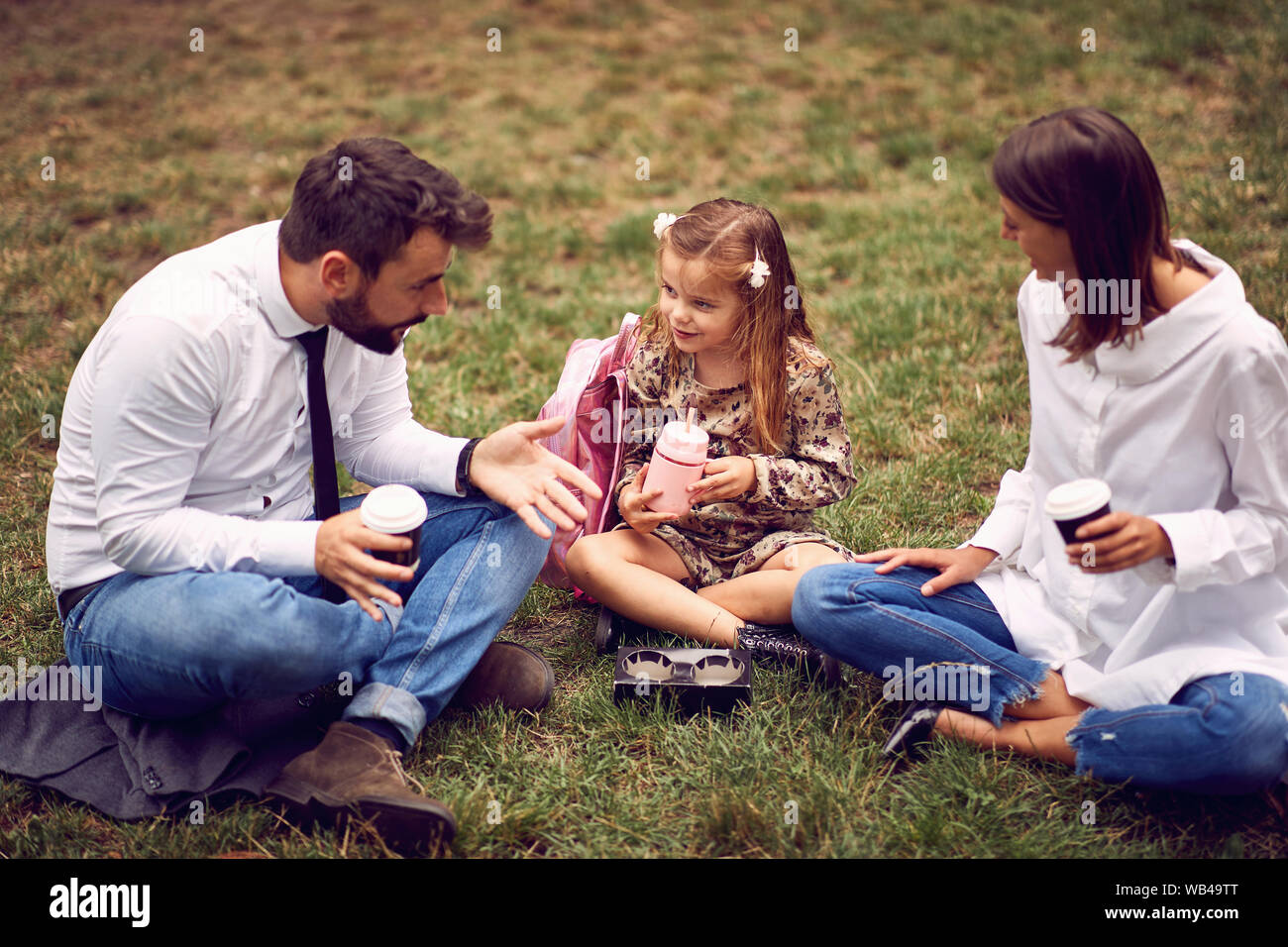 Felice genitore con la loro figlia dopo il lavoro e la scuola seduto e appoggiato al parco. Foto Stock