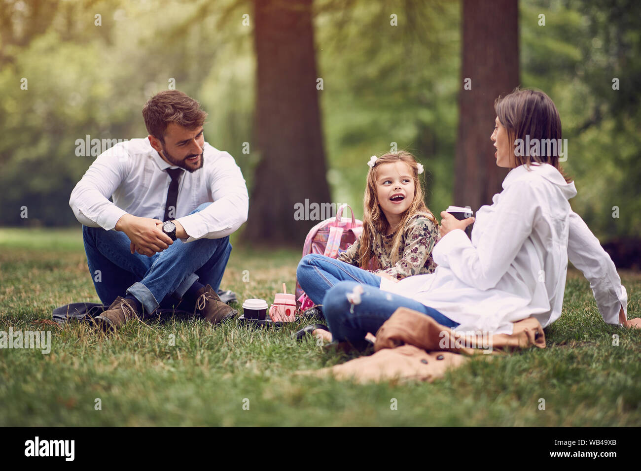 Felice famiglia giovane dopo il lavoro e la scuola seduto e appoggiato al parco. Foto Stock