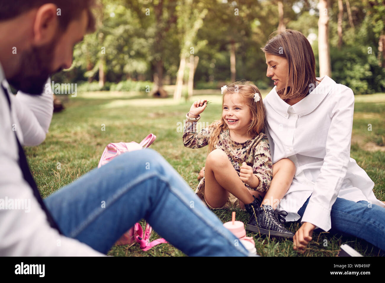 Carino figlia con la loro madre e padre seduto e appoggiato al parco. Foto Stock