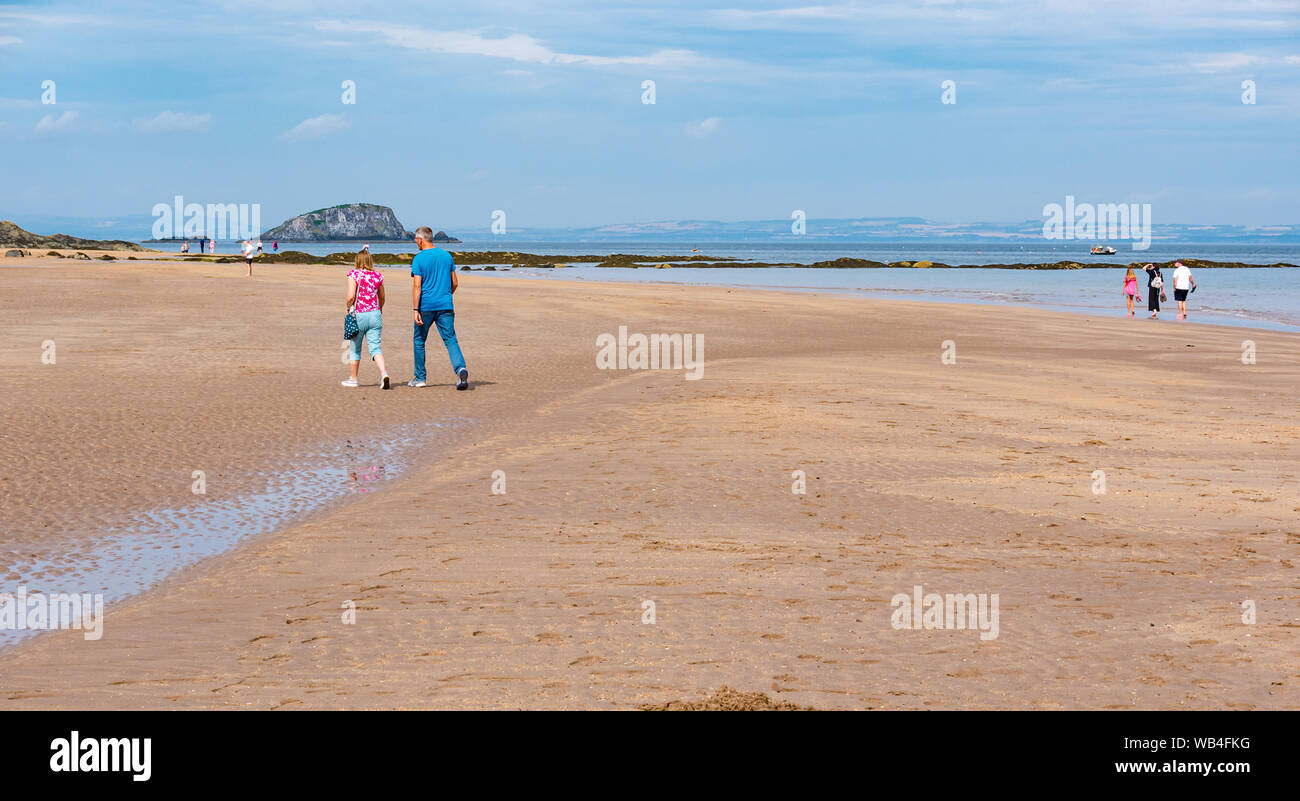 A North Berwick, Scozia, Regno Unito, 24 agosto. Regno Unito: Meteo persone godere il caldo sole di West Beach nella località balneare con la bassa marea. Un giovane alking sulla spiaggia con agnello Isola del Firth of Forth a distanza Foto Stock