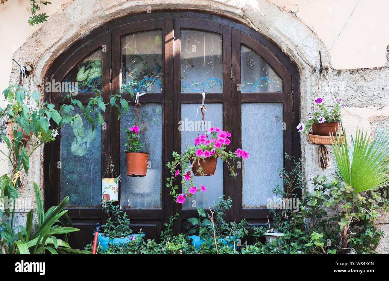 Un rustico di finestra in legno è circondato da vasi per piante e fiori in un colorato e casa felice in scena a Rethymnon, Creta Foto Stock