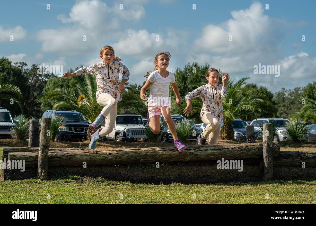 Tre giovani ragazze caucasiche sono saltando su un registro insieme ad uno spettacolo di cavalli durante l'attesa per i loro compagni di squadra per competere Foto Stock