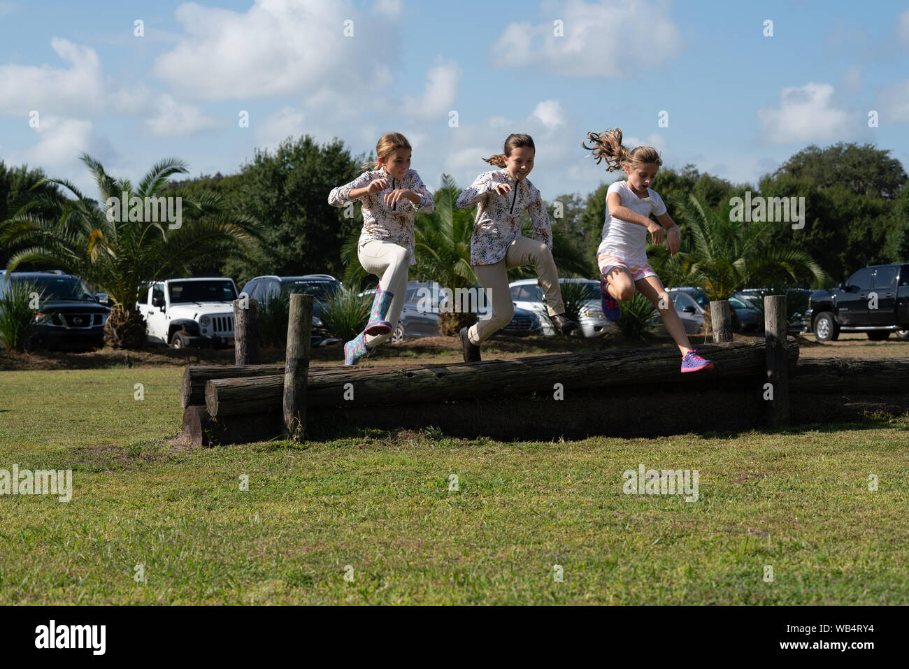 Tre giovani ragazze caucasiche sono saltando su un registro insieme ad uno spettacolo di cavalli durante l'attesa per i loro compagni di squadra per competere Foto Stock