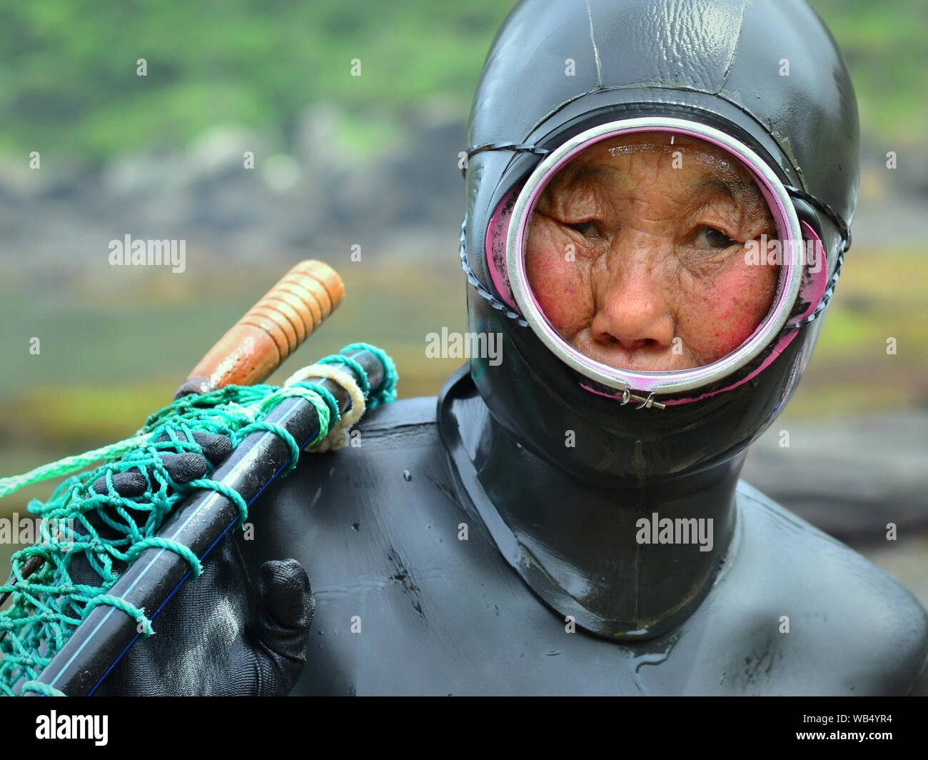 Esaurito il sud coreano di libero-diving nonna (haenyeo) indossa una vecchia maschera subacquea e una gomma usurata dry suit con il cofano. Foto Stock