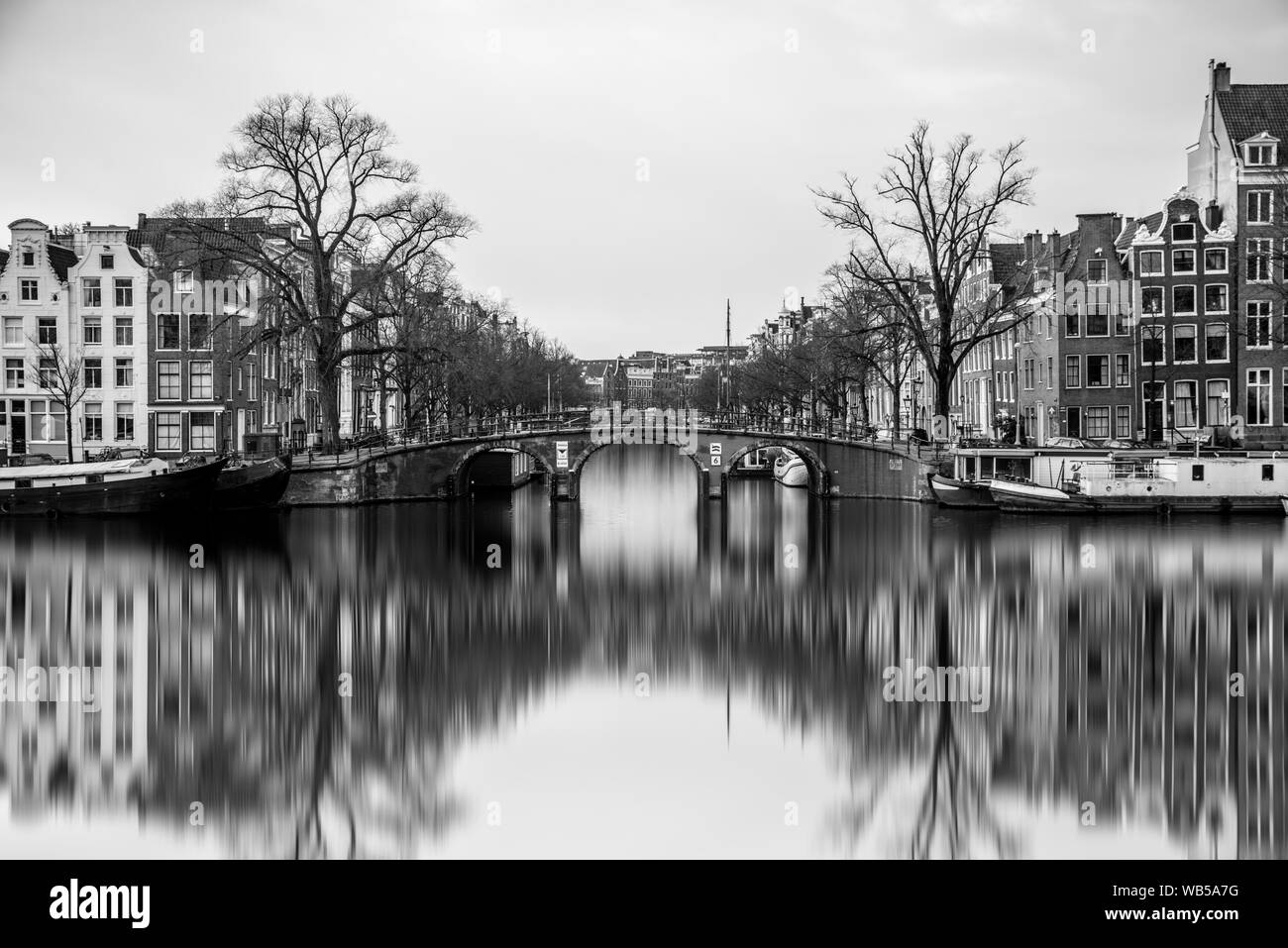 In bianco e nero lunga esposizione vista da Jan Vinkbrug sopra l'acqua nel fiume di Amsterdam Amstel durante l autunno su un luminoso giorno con boathouses e re Foto Stock