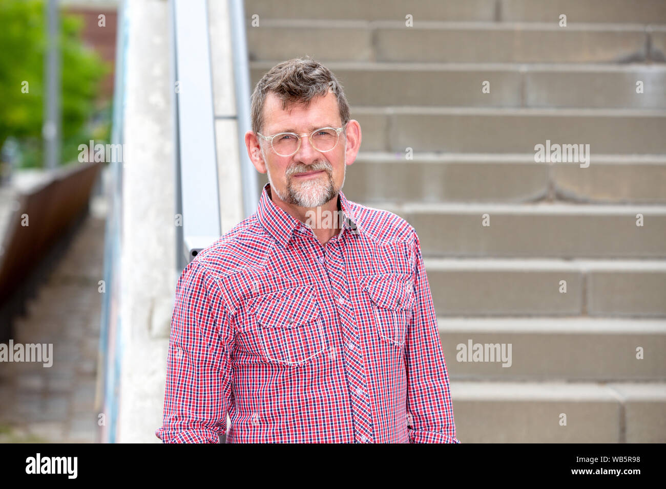 Ritratto di uomo bello nella sua 50s con maglietta plaided permanente al scale Foto Stock