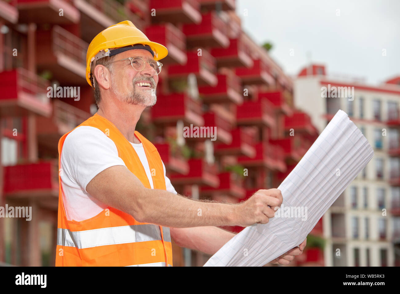 Ritratto di bello il lavoratore nel suo 50s con casco fuori e tenendo un piano Foto Stock