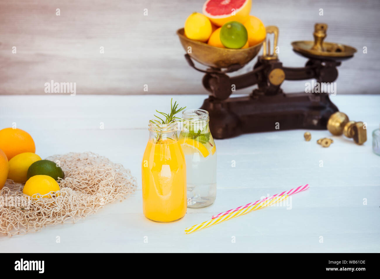 Due bottiglie con limonata fatta in casa e arancione del succo di frutta fresco con la menta e il ghiaccio sul bianco sullo sfondo di legno con agrumi freschi in scala vintage e alcuni Foto Stock