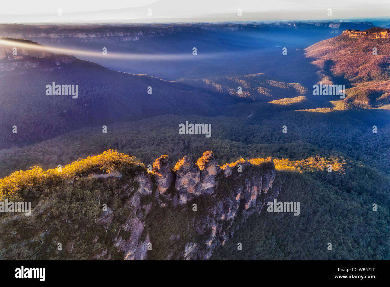 Sun raggi di luce e haze spunto al Grand Canyon in montagne blu in Australia oltre la formazione rocciosa Tre Sorelle visto da sopra durante il sun Foto Stock