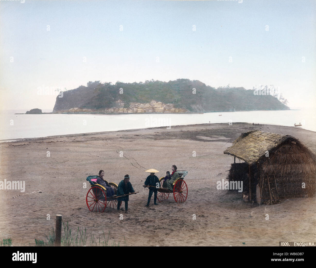 [ 1890 Giappone - Isola di Enoshima ] - isola di Enoshima in Sagami Bay, nella prefettura di Kanagawa. Due jinrikisha (rickshaws) con estrattori e i passeggeri possono essere visti in primo piano, accanto a un piccolo capannone. La piccola isola con una circonferenza di appena 4 km è stata collegata alla terraferma durante la bassa marea, ma potrebbe essere raggiunta solo in barca durante l'alta marea. Xix secolo albume vintage fotografia. Foto Stock