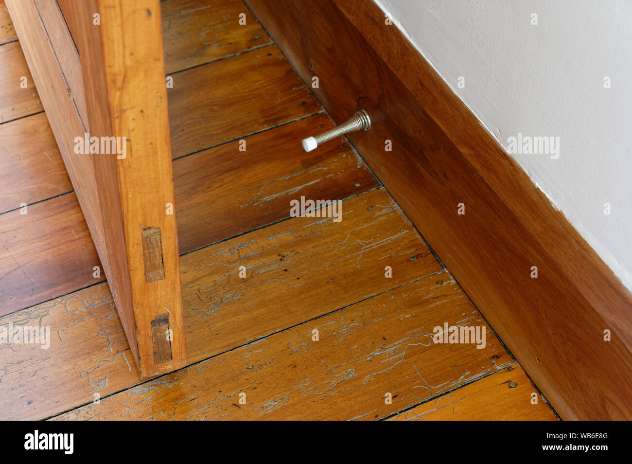 Una porta di legno è impedito di colpire la parete da una molla in metallo porta tappo attaccato al battiscopa Foto Stock