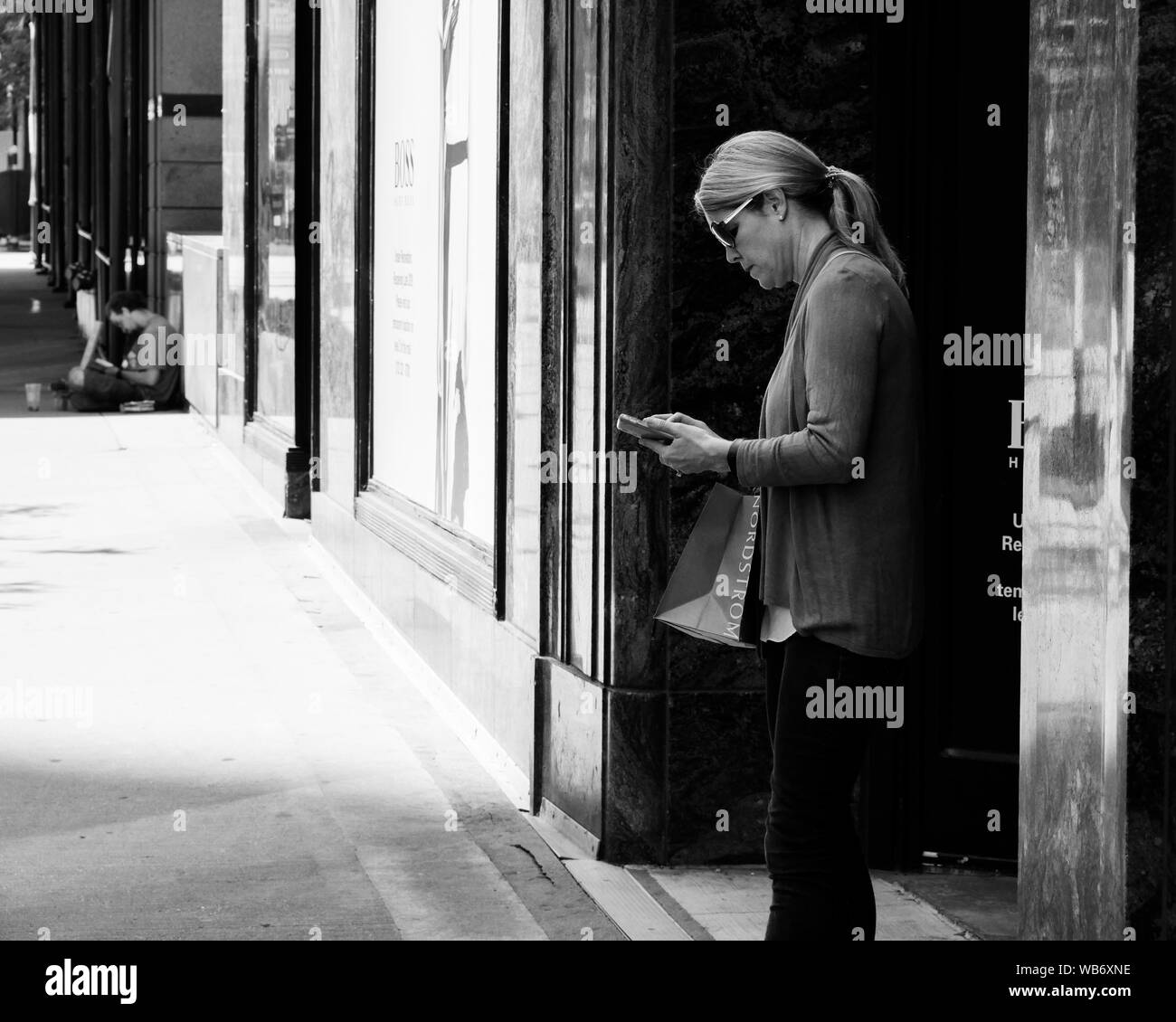 Donna con Nordstrom del sacco controllo telefono. Senzatetto in background. Chicago, Illinois. Foto Stock