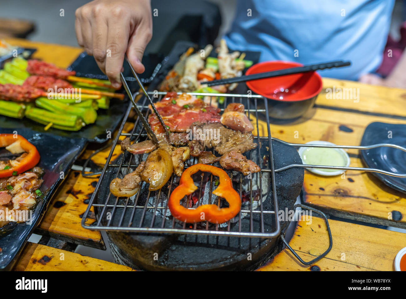 L uomo per grigliare le fette di carne e peperone su stufa a carbone Foto Stock