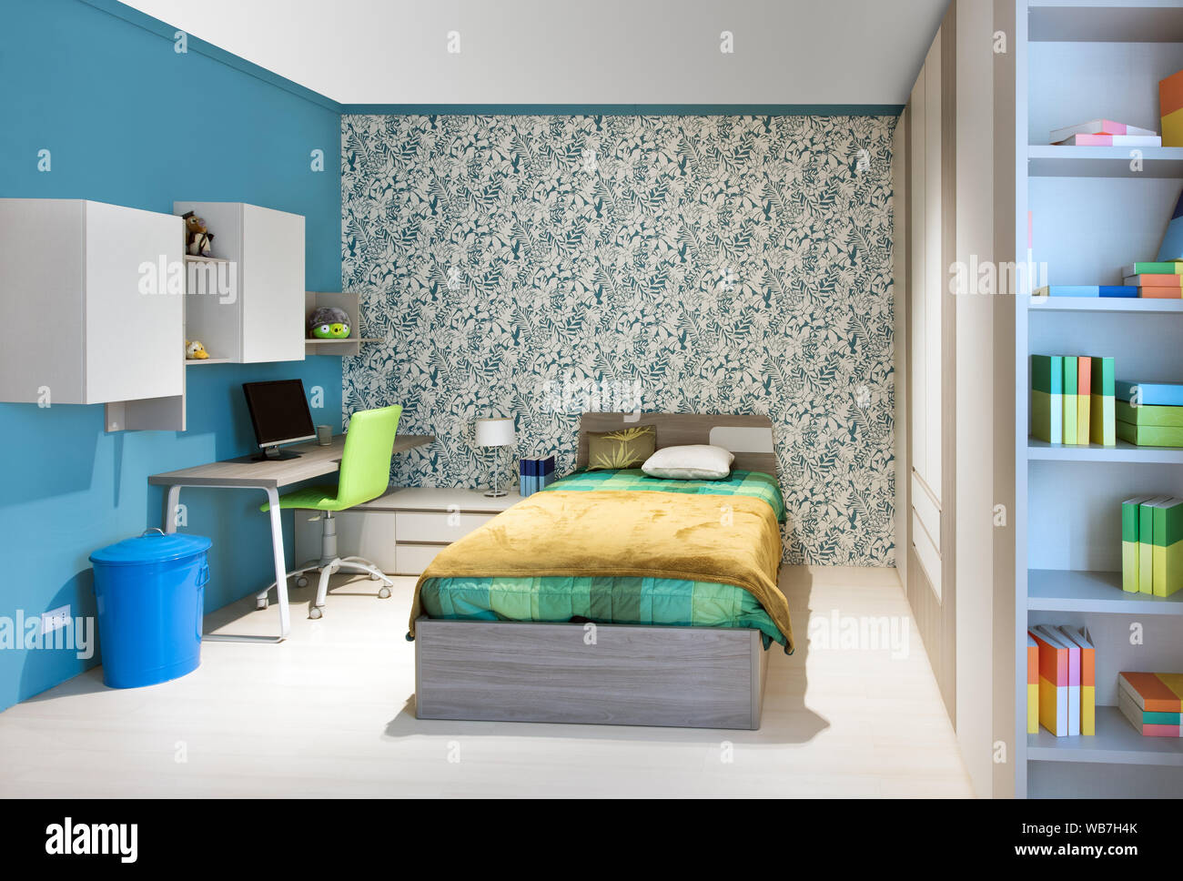 Neat adolescenti camera con decorazioni blu, dotato di unità a parete e una piccola scrivania accanto a un divano letto singolo con funzione wallpaper Foto Stock