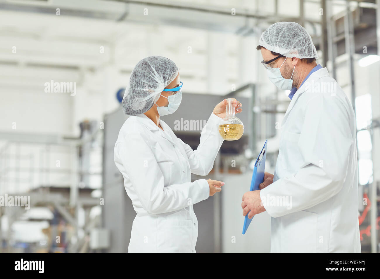 Lavoratore in maschere e cappotti guardare il liquido nel pallone a lavoro. Foto Stock