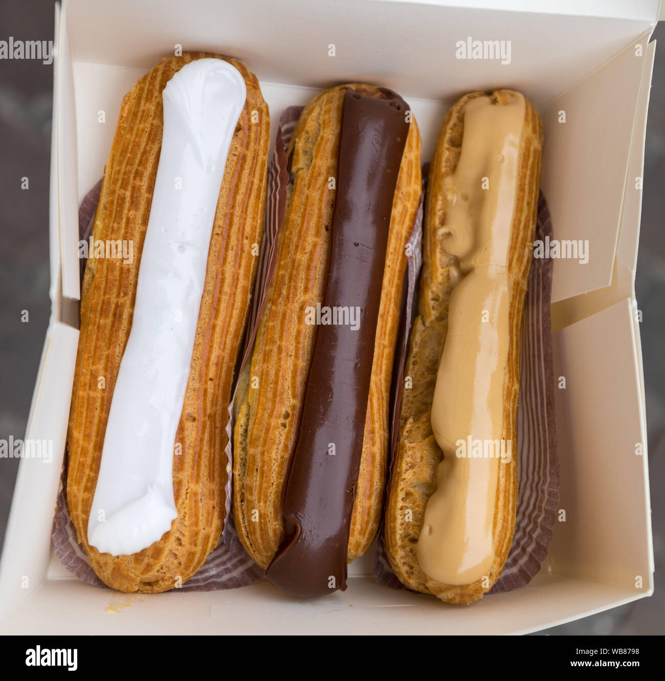 Eclairs colorato nella casella . Eclairs recante all'interno di caselle bianche. Eclair torte con scottate Carmelo e Caffè crema di burro. Foto Stock