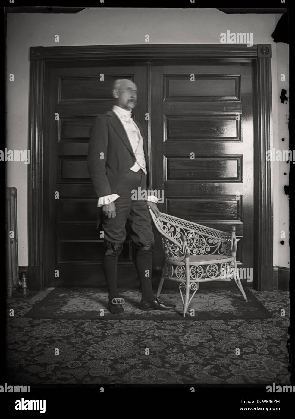Uomo in piedi accanto ad una sedia di vimini, indossando coloniale storico con lo stile del periodo di vestiti. Scansione di originali dalla lastra di vetro negativo circa primi 1900s. Foto Stock