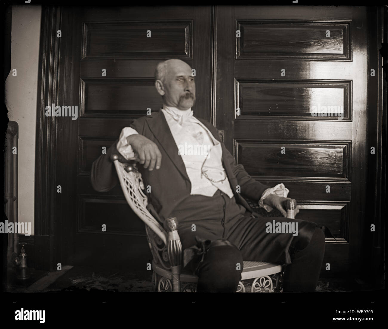 Uomo in una sedia di vimini, indossando coloniale storico con lo stile del periodo di vestiti. Scansione di originali dalla lastra di vetro negativo circa primi 1900s. Foto Stock