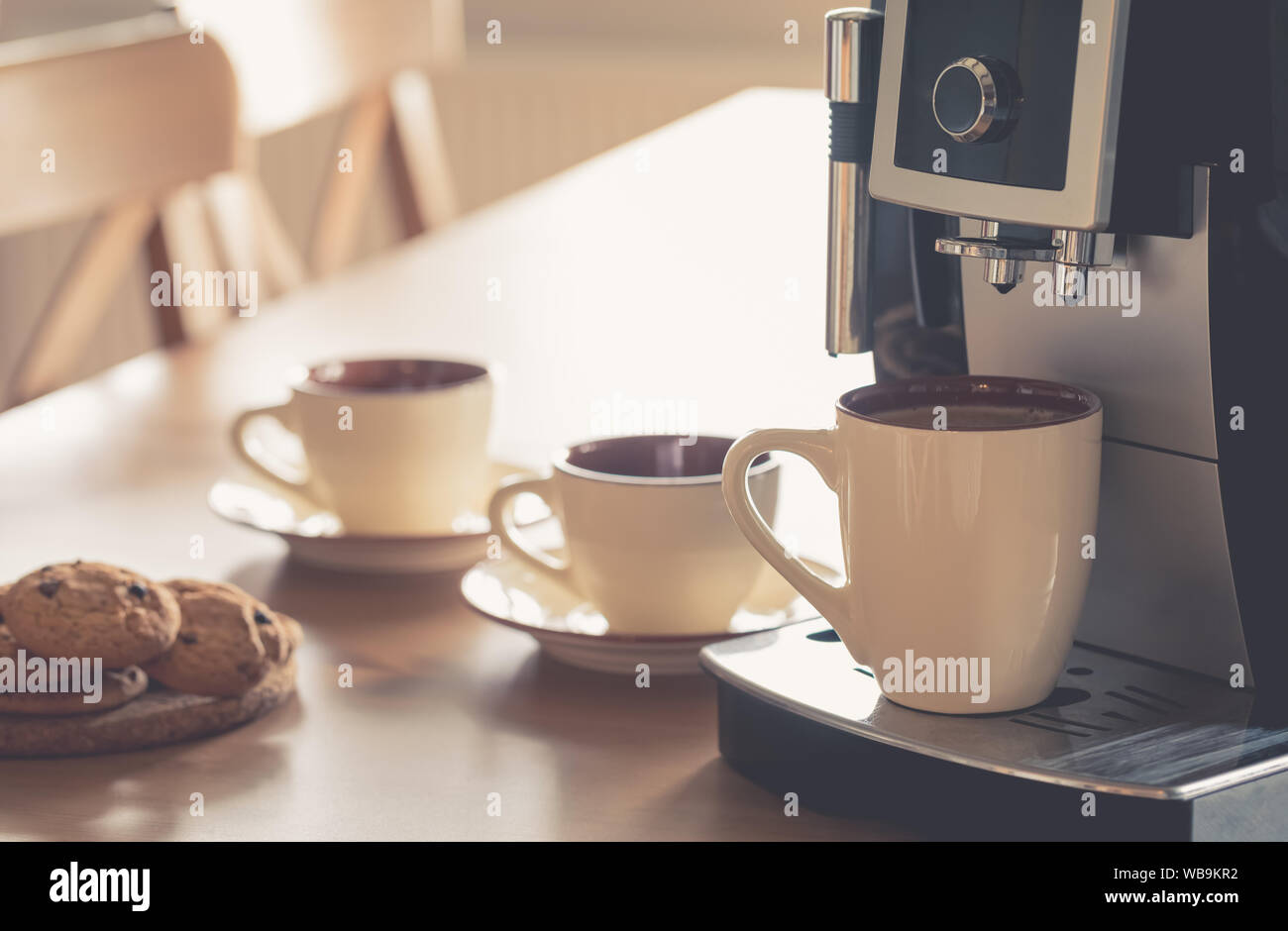 Tazze di caffè espresso mattutino nella macchina per caffè con biscotti sul tavolo di legno, tonica Foto Stock