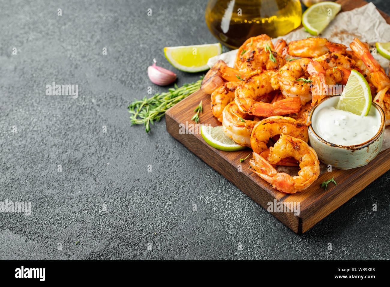 Gamberi o gamberi grigliati serviti con lime, aglio e salsa bianca su fondo di cemento scuro. Frutti di mare. Con spazio di copia Foto Stock