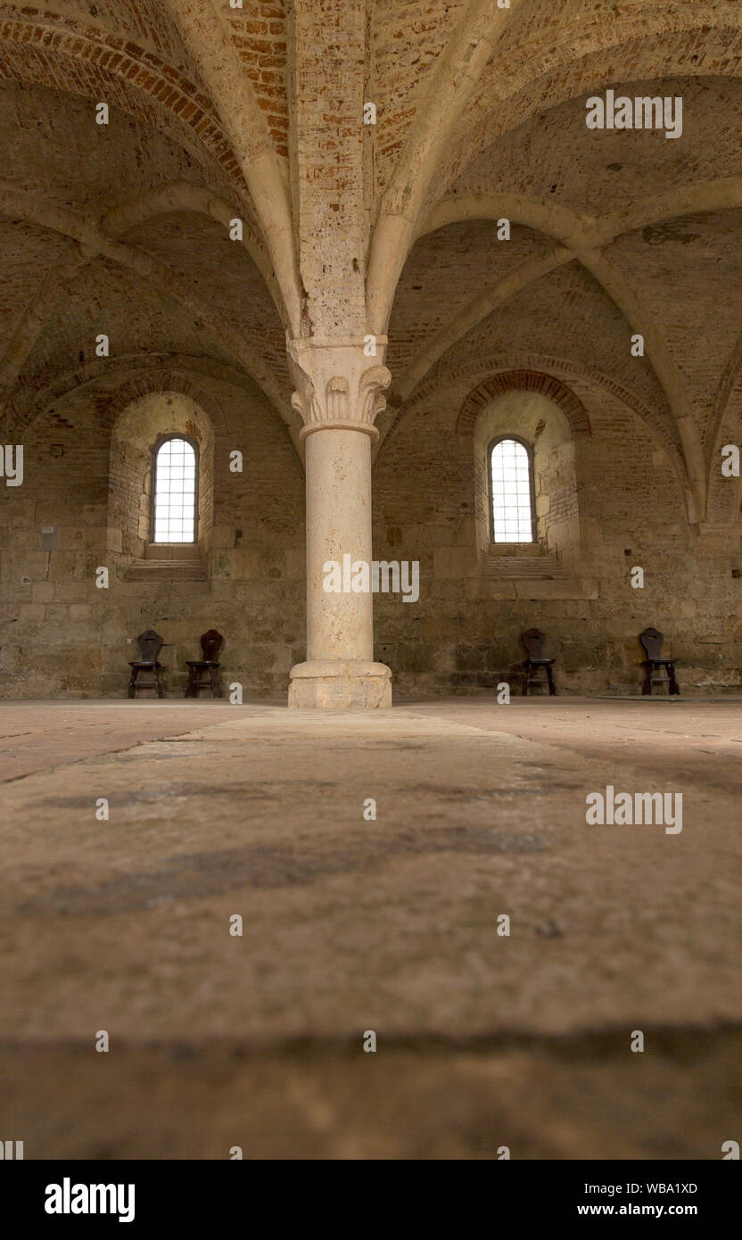 Lo spazio interno all'Abbazia di San Galgano di Chiusdino, Italia. Prospettiva bassa i pavimenti in pietra e soffitti a volta; vecchie sedie in distanza. Foto Stock