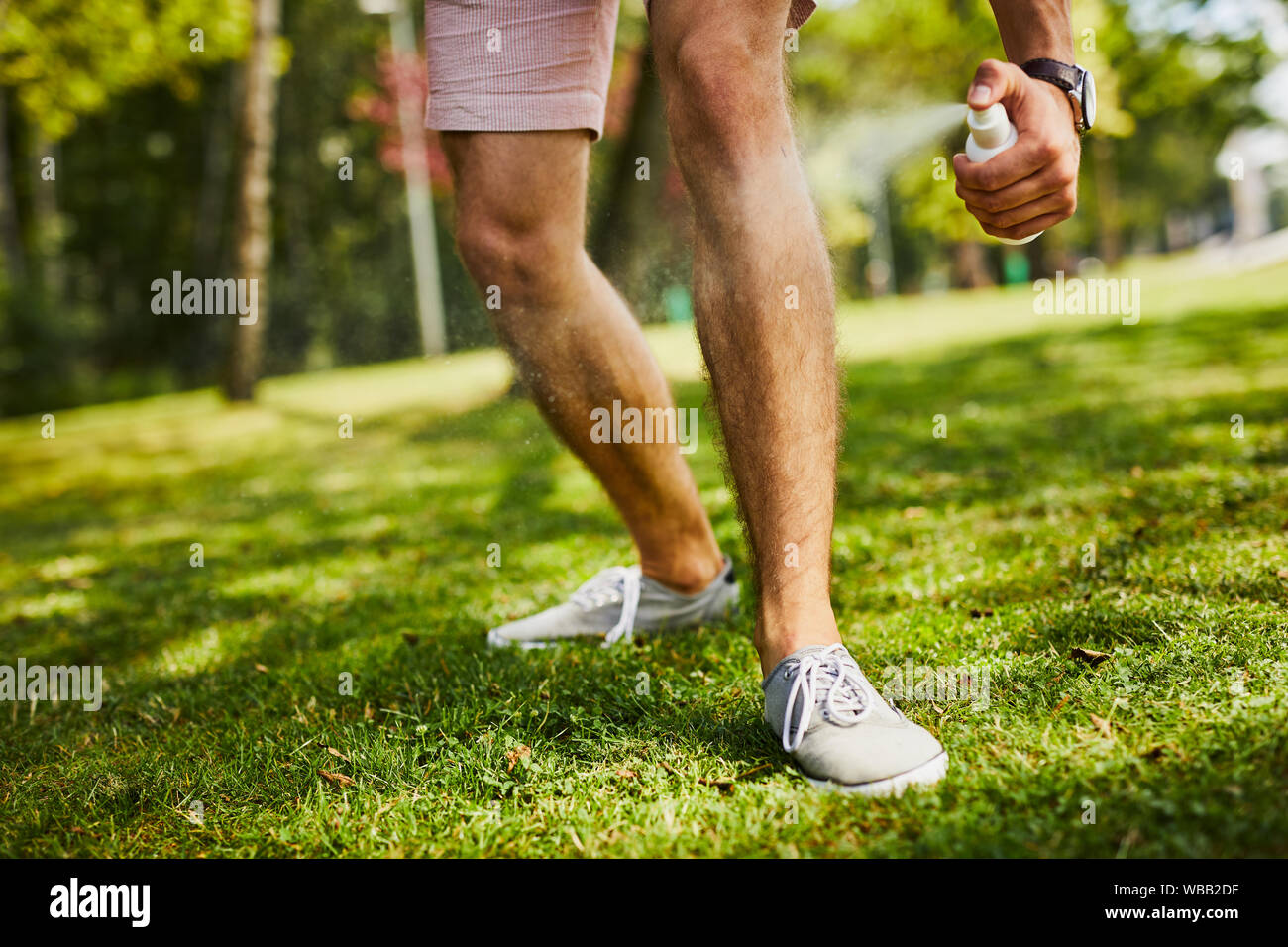 Close-up di uomo di gambe essendo spruzzato con repellente per insetti nel parco all'aperto Foto Stock