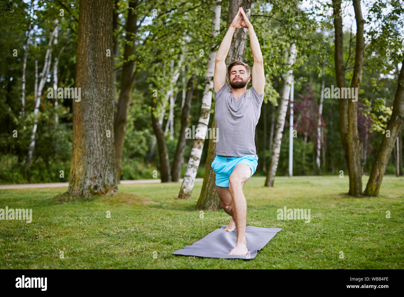 Focalizzato giovane uomo fare yoga pone nel parco di mattina Foto Stock