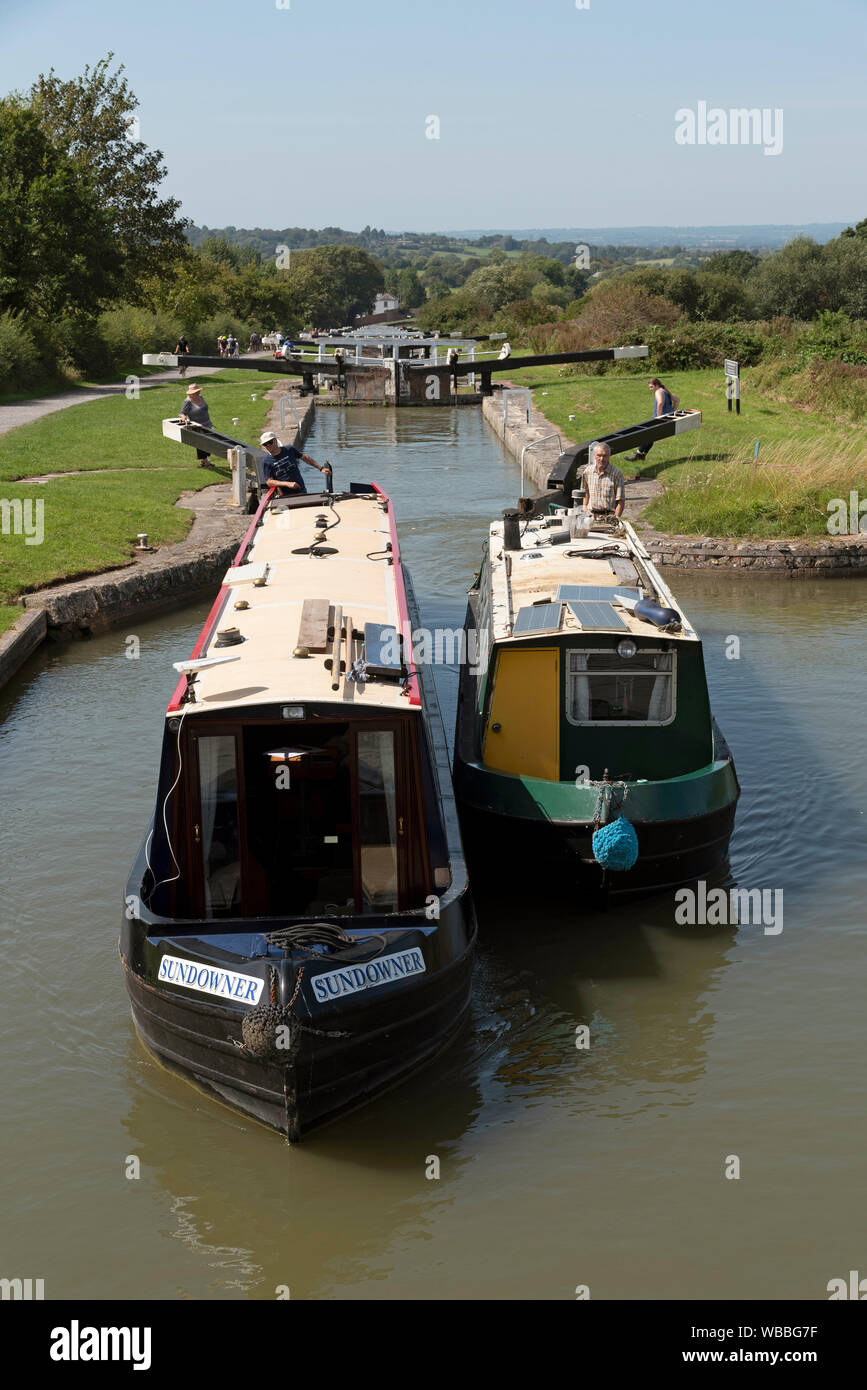 Devizes, Wiltshire, Inghilterra, Regno Unito. Agosto 2019. Due narrowboats viaggiare insieme attraverso uno dei blocchi sulla collina di Caen volo delle serrature. Foto Stock