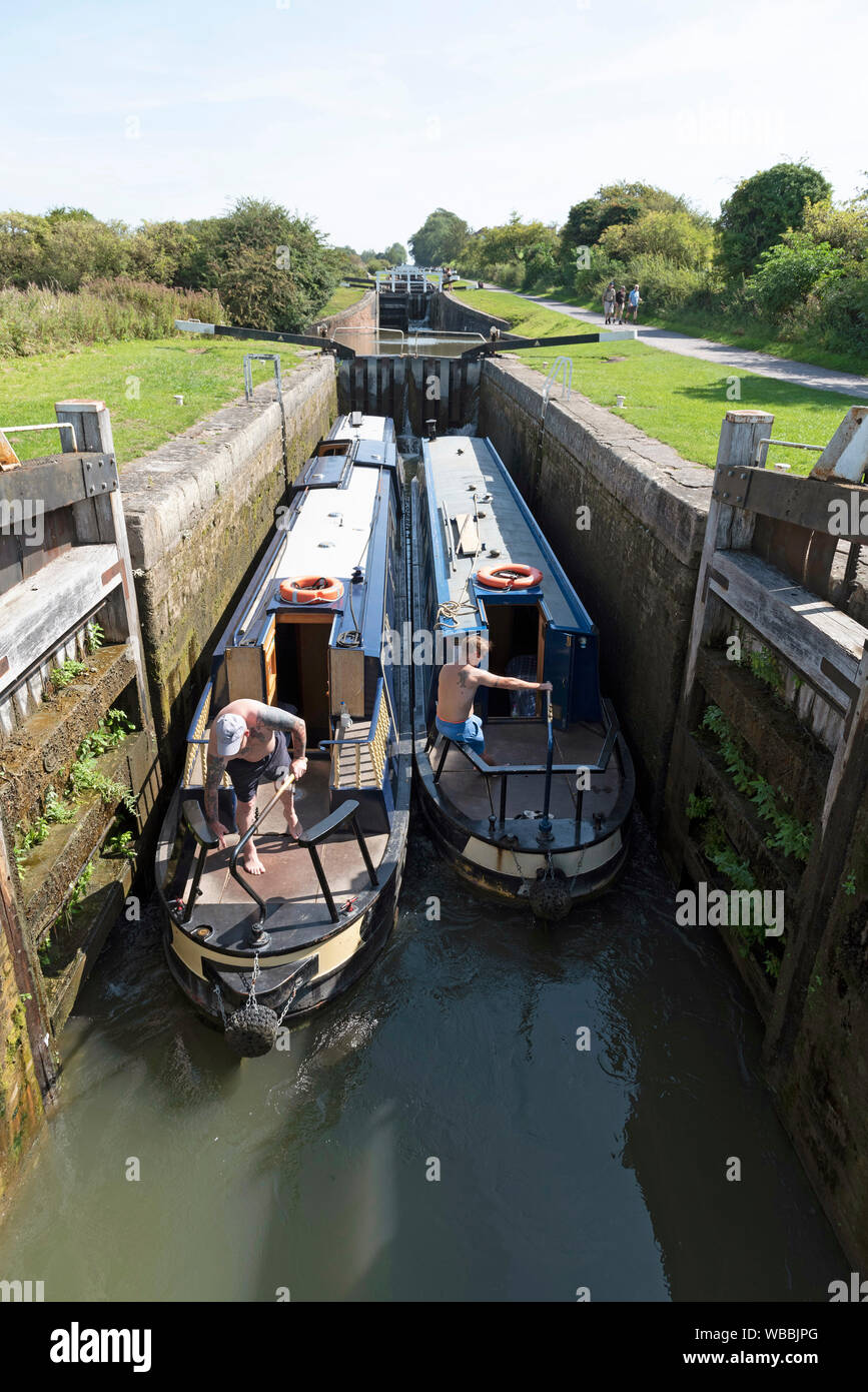 Devizes, Wiltshire, Inghilterra, Regno Unito. Agosto 2019. Due narrowboats viaggiare insieme attraverso uno dei blocchi sulla collina di Caen volo delle serrature. Foto Stock