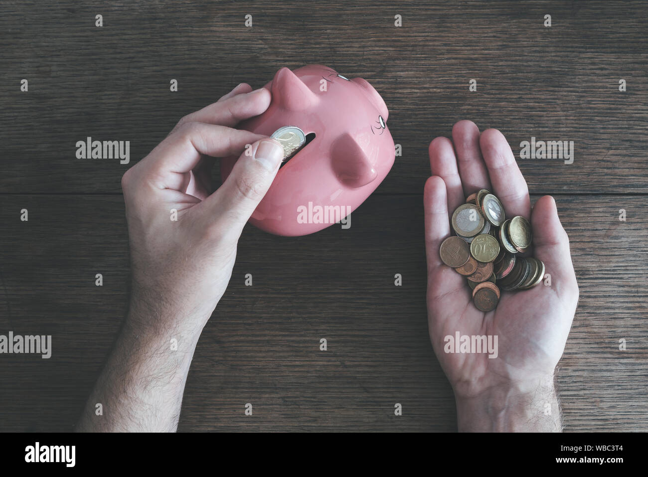 Vista superiore dell uomo con monete in una mano e mettere il denaro nel salvadanaio con l'altra mano, risparmiando denaro concept Foto Stock