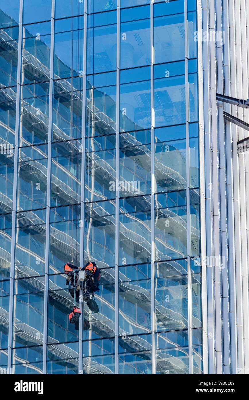 Due uomini che si abbellono o si abbellono e lavorano su una tenda di vetro all'esterno di una nuova torre per uffici a più piani a Sydney, Australia Foto Stock