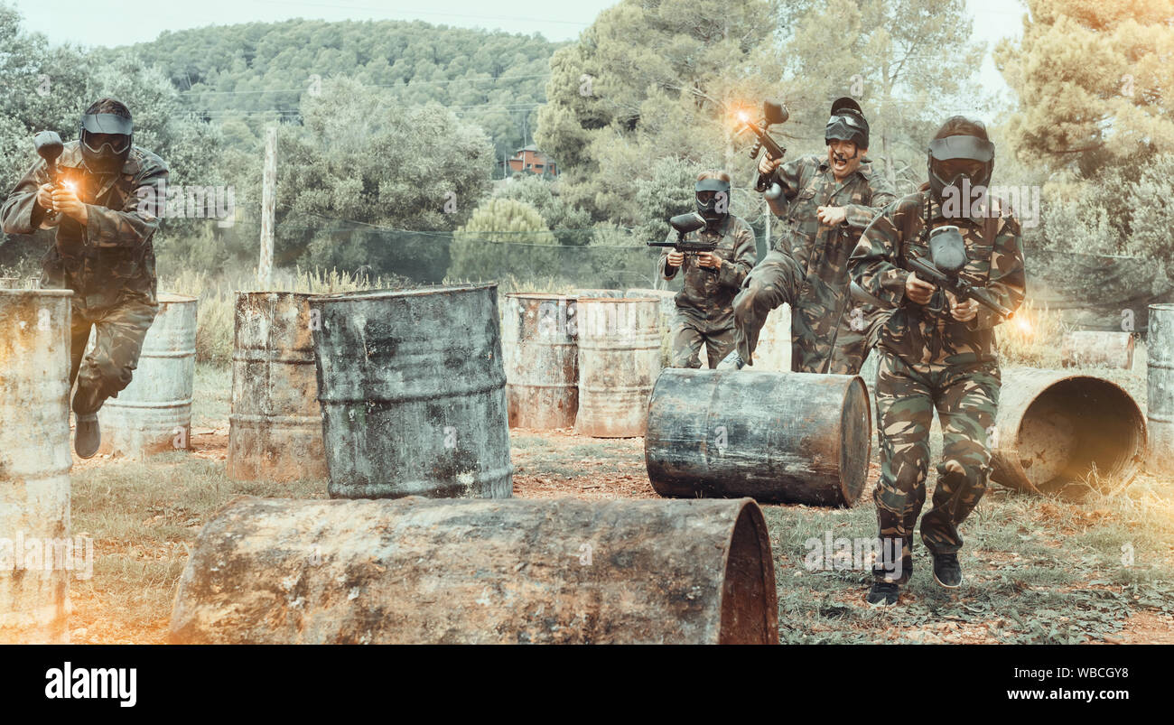 Dynamic paintball battaglia. Gruppo di maschi e femmine in pieno il paintball attrezzature attaccando squadra opposta Foto Stock